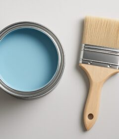 A can of blue paint and a paintbrush on a light background.