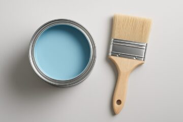 A can of blue paint and a paintbrush on a light background.
